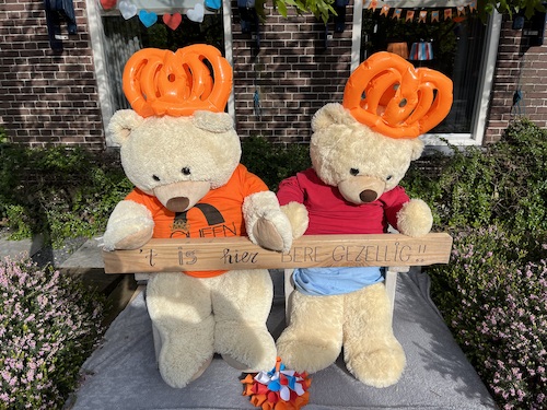 2 teddybeertjes in een versierde straat. Ze houden een balkje vast met de tekst: Het is hier bere-gezellig