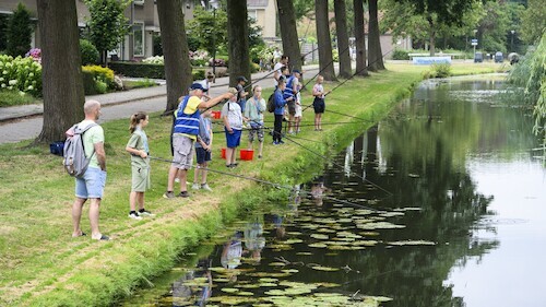 oudere man staat met jonge kinderen een vishengel te werpen